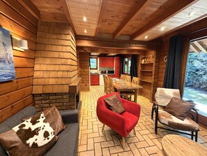 A cozy cabin interior with a fireplace, wooden walls, a dining area, and a view of the outdoors.