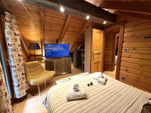 A wooden cabin room with a bed, a chair, a television, and a wardrobe.