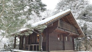 A wooden cabin with a balcony, surrounded by snow-covered trees. - LE MONTAGNARD Chalet en bois (La Bresse)