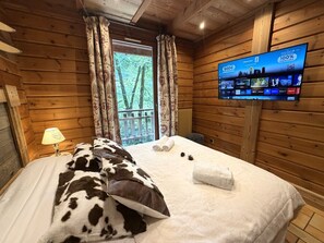 A wooden cabin room with a bed, a TV, and a window with curtains.