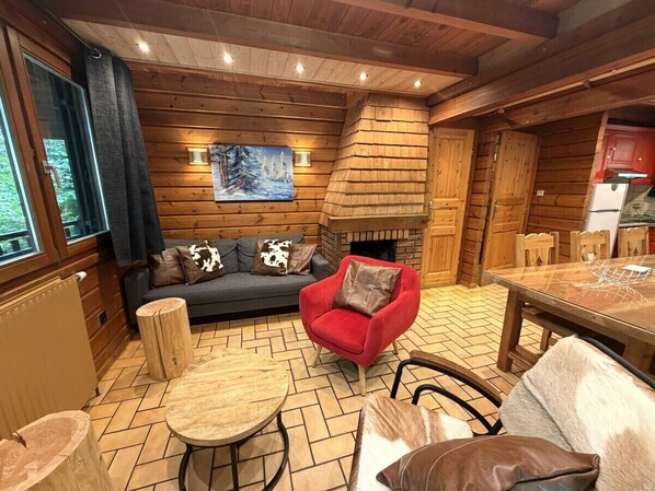 A cozy cabin interior with a sofa, red armchair, wooden flooring, and a fireplace.