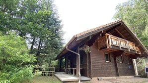 A wooden cabin with a balcony, surrounded by trees.