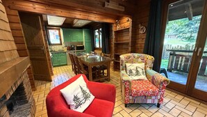 A cozy cabin interior with a fireplace, a dining area, and a view through a glass door.