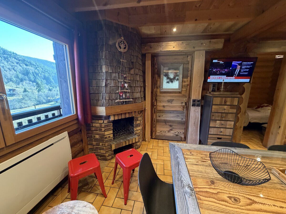 L’intérieur chaleureux d’un chalet avec une cheminée en pierre, un téléviseur et une table à manger en bois.