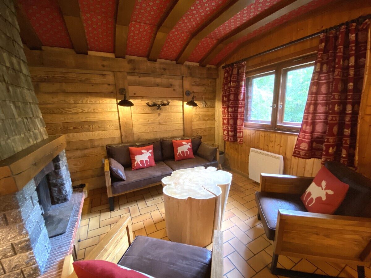 A cozy log cabin interior with a stone fireplace, wooden furniture, and a window with patterned curtains.
