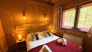 A wooden cabin bedroom with a bed, two nightstands, a window with curtains, and a red blanket.