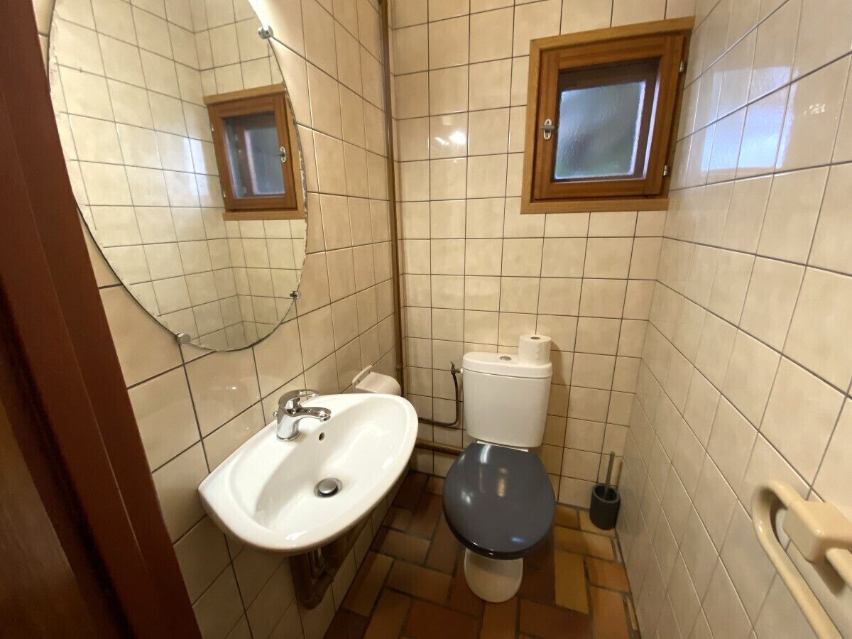 A small bathroom with a white sink, a toilet, and a window above the toilet.