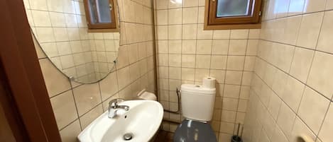 A small bathroom with a white sink, a toilet, and a window above the toilet.