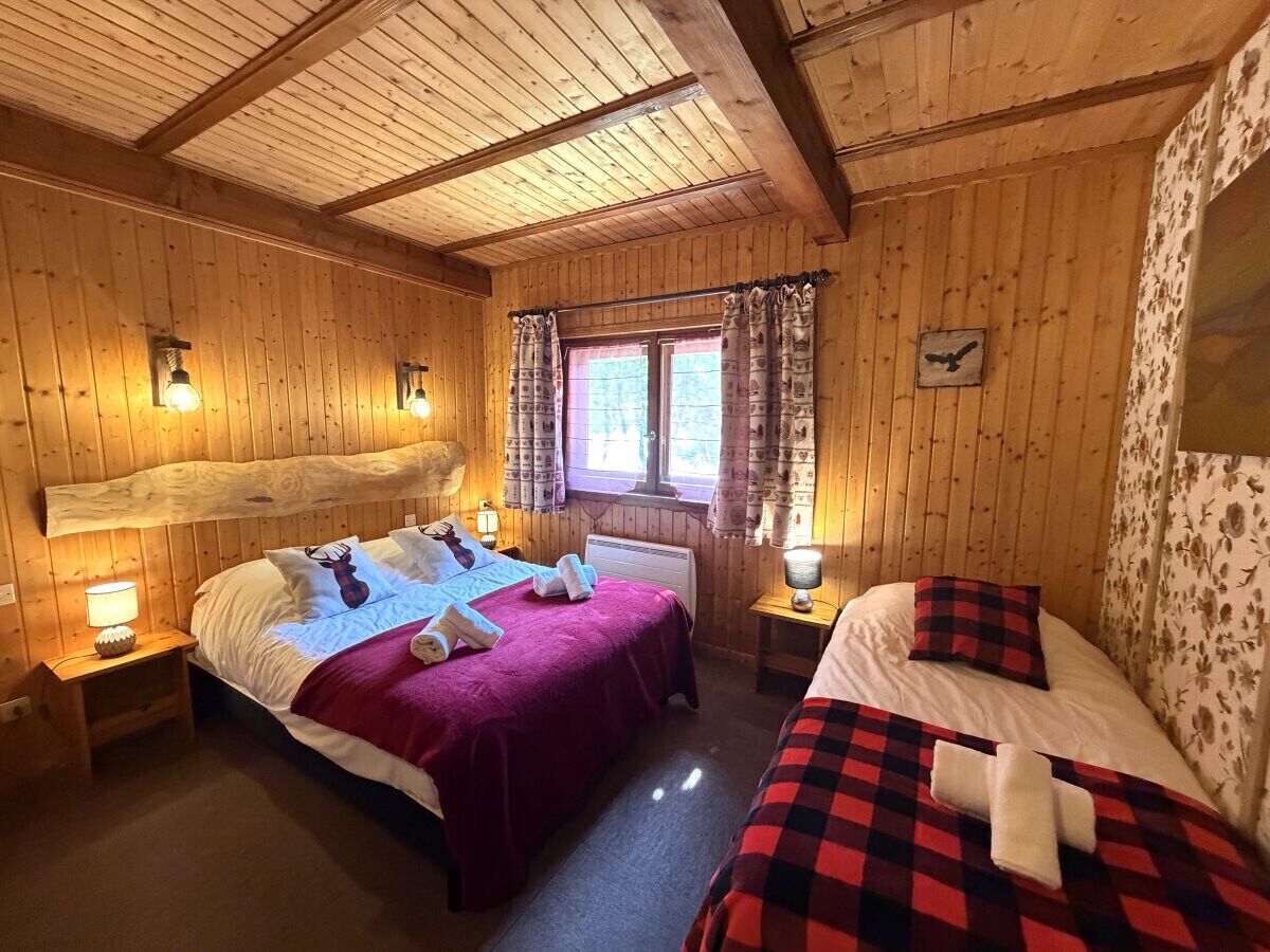 A wooden cabin with two beds, a window with curtains, and a wall-mounted clock.