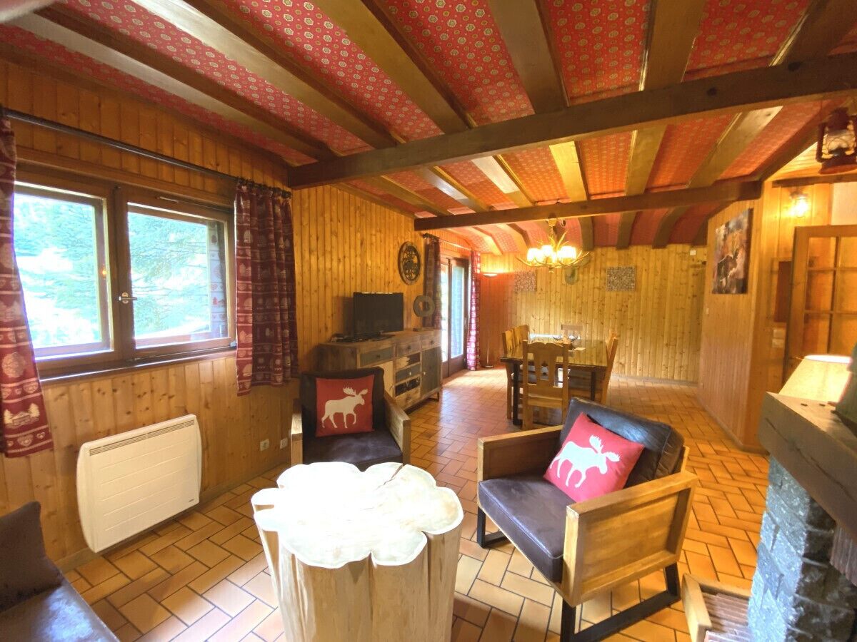 Een gezellig chaletinterieur met houten wanden, een open haard, een eethoek en een zithoek met een tafel en stoelen.