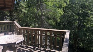 A wooden deck with a table and chairs, surrounded by dense trees.