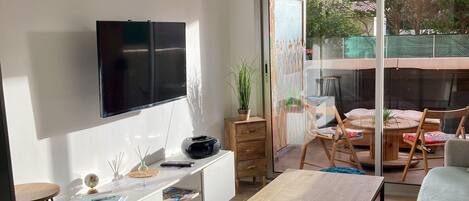 Un salón moderno con televisor de pantalla plana, una mesa de centro de madera, un otoman azul y una lámpara colgante de mimbre.