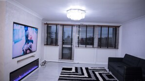 A living room with a flat-screen TV, a fireplace, a black sofa, and a patterned rug. - Stunning 2-bed Apartment in London (London)