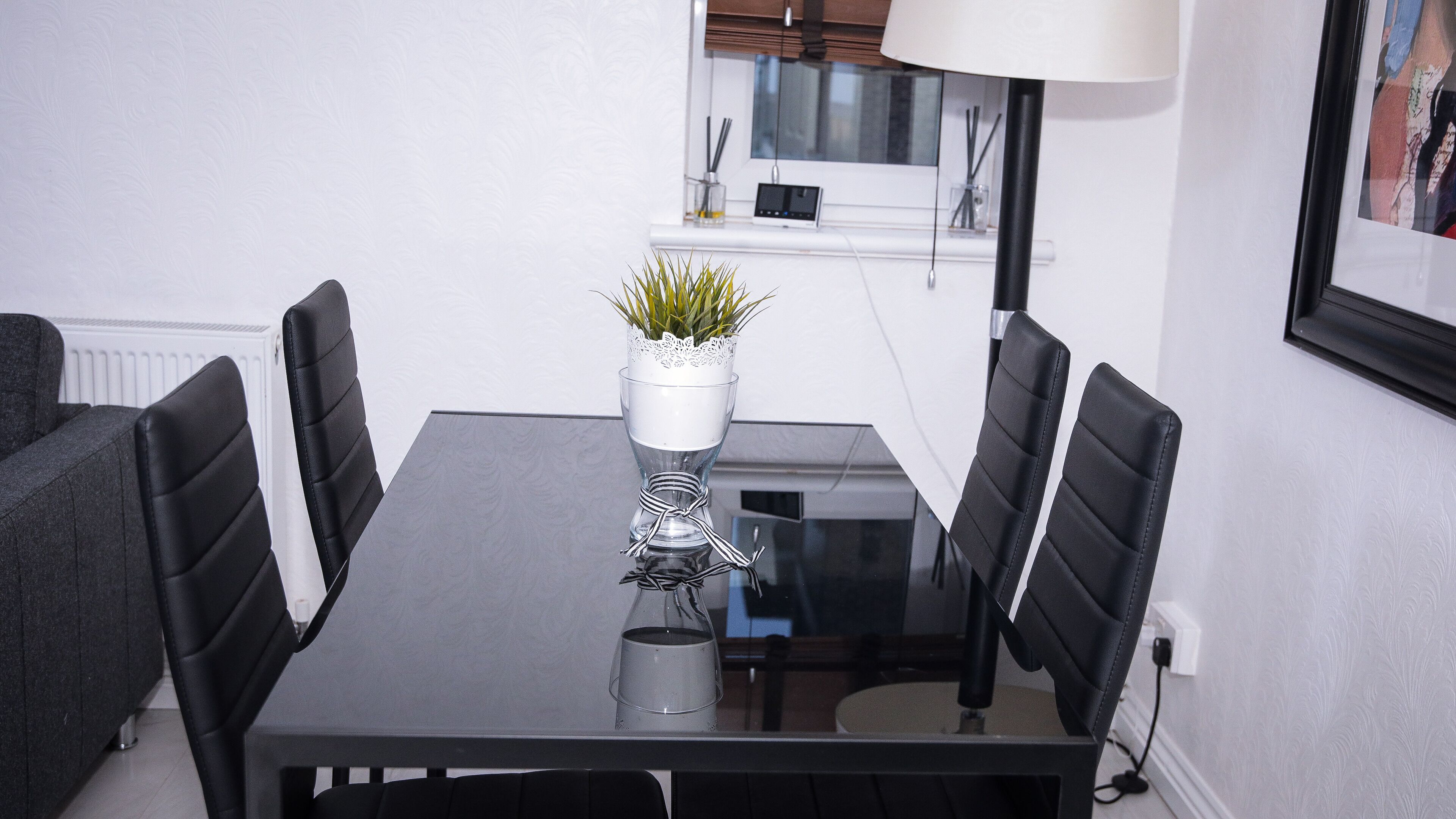 A modern dining area with a glass table, black chairs, and a potted plant centerpiece.