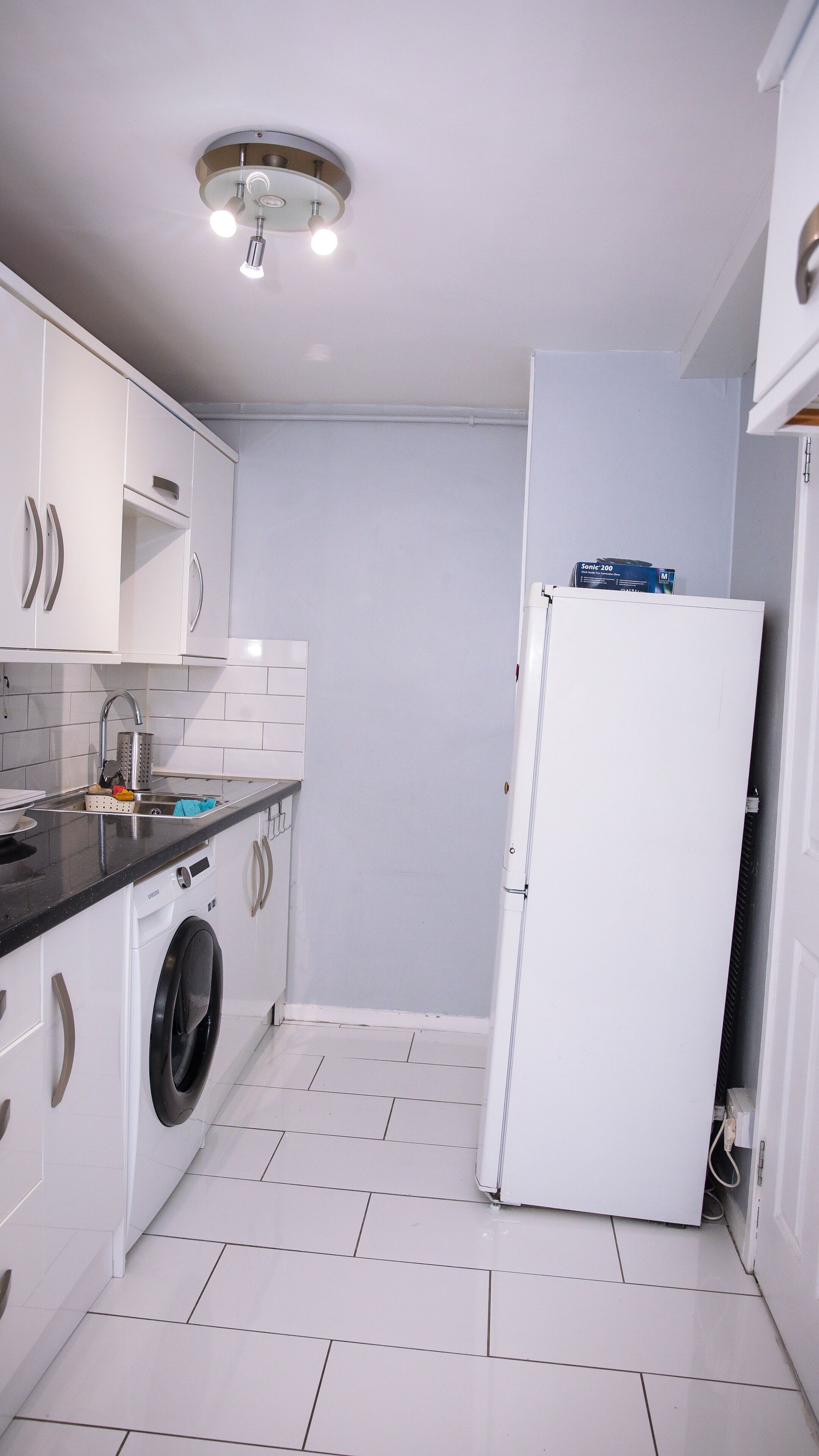 A compact kitchen with white cabinets, a washing machine, a refrigerator, and a ceiling light fixture.