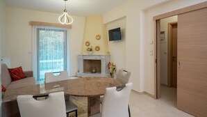 A dining area with a round table, chairs, a fireplace, and a TV mounted on the wall. - The Miller House under Meteora (Kalampaka)