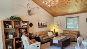 Una sala de estar acogedora con techo de madera, un sofá de cuero blanco, un sillón reclinable blanco y una mesa de centro de madera.