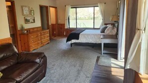 Un dormitorio con cama, cómoda, sofá de cuero marrón y un ventanal grande.