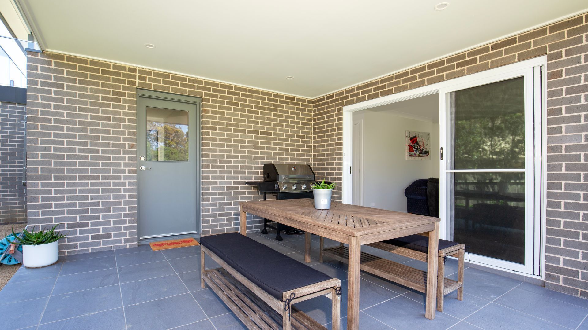 A patio with a wooden table and bench, a barbecue grill, and a sliding glass door.