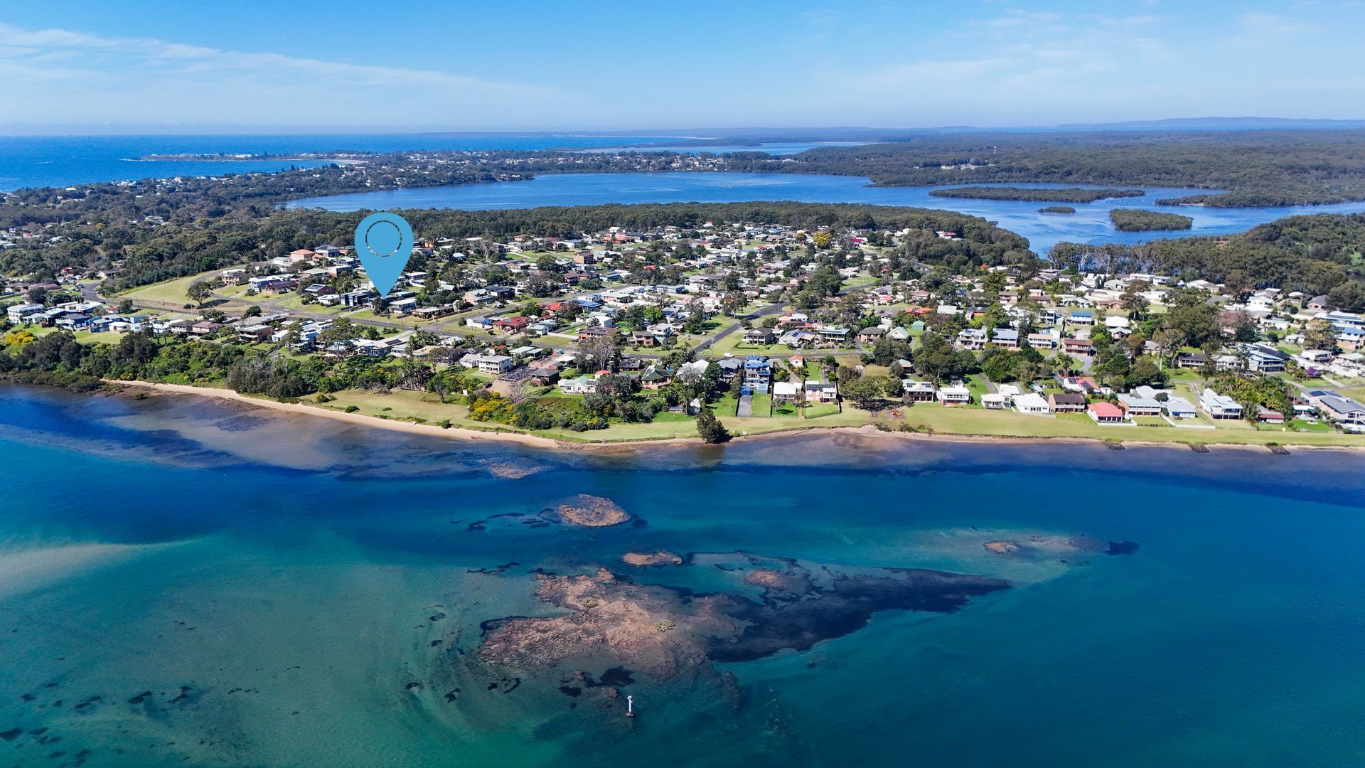Oversigtsbillede af et kystnært boligområde med huse, en strand og klart, blåt vand.