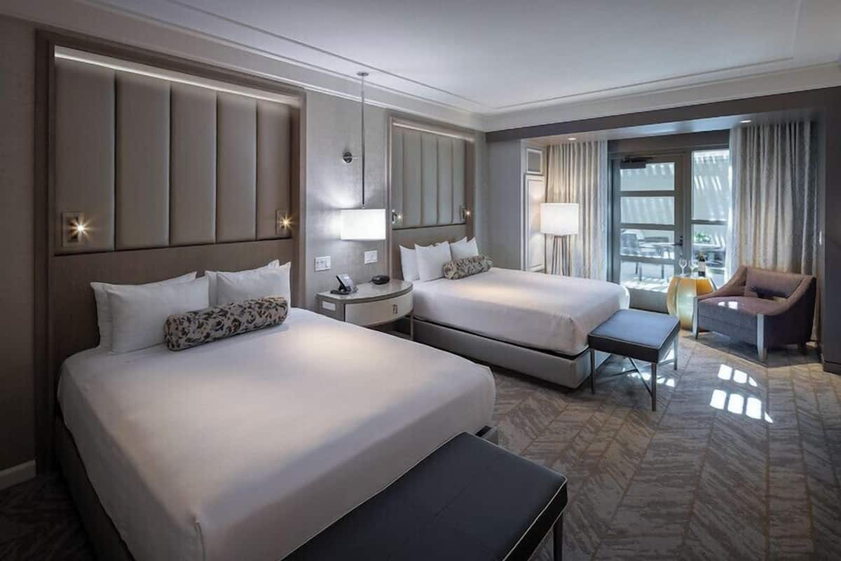Una habitación de hotel con dos camas, un escritorio, una silla y vistas amplias por un ventanal.