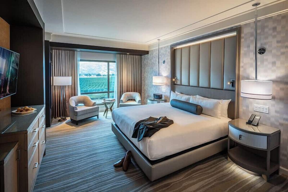 Habitación de hotel con una cama grande, televisión, escritorio, silla y vista al exterior.