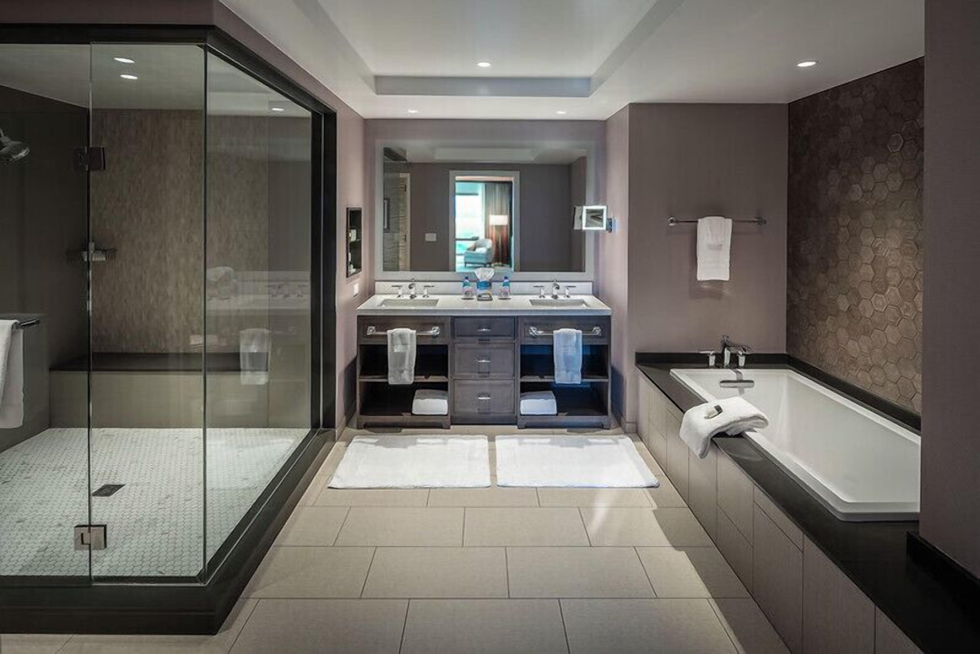 A modern bathroom with a glass shower enclosure, a large bathtub, a vanity with a mirror, and a tiled floor.