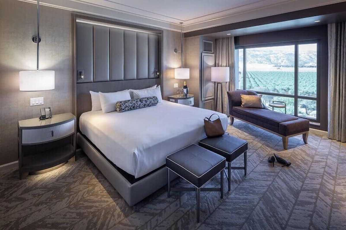 Una habitación de hotel con una cama grande, mesitas de noche, un sofá y vistas al exterior.