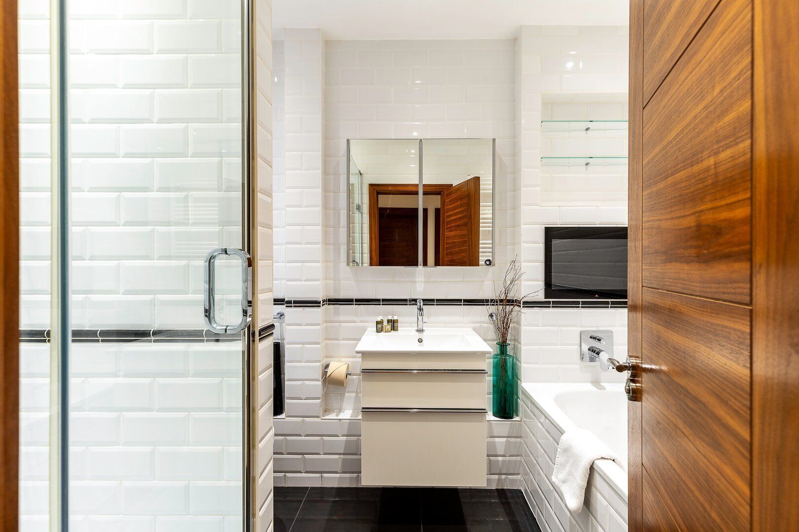 Une salle de bain moderne avec une douche à parois de verre, un lavabo blanc avec un miroir au-dessus et une porte en bois.