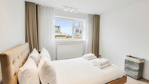 Ein modernes Hotelzimmer mit einem großen Bett, Blick auf Gebäude durch das Fenster und einem grauen Schrank.