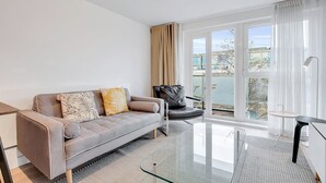 Ein modernes Wohnzimmer mit einem grauen Sofa, einem schwarzen Sessel und einem Glastisch.