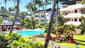 Een resort met een zwembad, omringd door palmbomen en weelderige begroeiing.