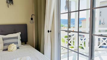 A bedroom with a bed, a headboard, a hanging light fixture, and a view through a large window to an outdoor balcony.