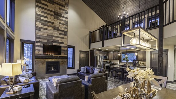 A spacious living area with a fireplace, dark leather sofas, a dining table with a centerpiece, and a kitchen in the background. - Modern spacious 5 bedroom, 3.5 bath, paved roads, hot tub, wifi, pool access (Lead)