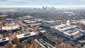 An aerial view of a cityscape with a mix of commercial and residential buildings, a large parking lot, and a distant skyline.