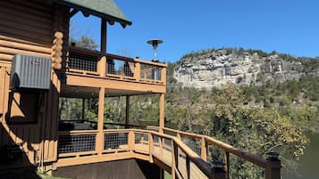 A wooden cabin with a balcony overlooking a lake and a rocky cliff.