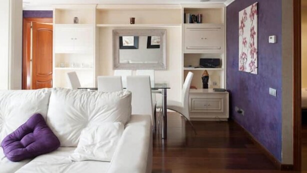 A modern living room with a white sofa, a purple pillow, a glass coffee table, and a white dining area with chairs. - Spectacular Five Senses Mallorca Apartment (Barcelona)