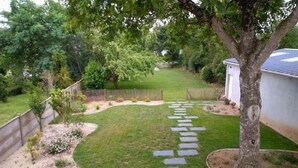 A backyard with a stone pathway leading to a wooden fence, surrounded by trees and a white building. - Ty Boca - Maison pour 6 avec jardin (Dinéault)