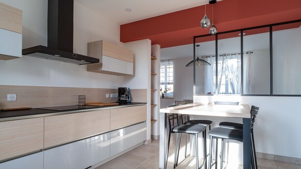 A modern kitchen with a central island, a black range hood, and a dining area with black chairs. - Ty Boca - Maison pour 6 avec jardin (Dinéault)