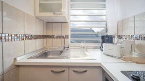 Una cocina moderna con un lavamanos de acero inoxidable, encimeras blancas y una ventana con persianas.
