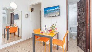 Una habitación compacta con una mesa de comedor, sillas, un espejo, un cuadro de una playa y una puerta de madera.