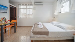 Habitación de hotel con cama, escritorio con sillas, ventana con cortinas translúcidas y aire acondicionado.