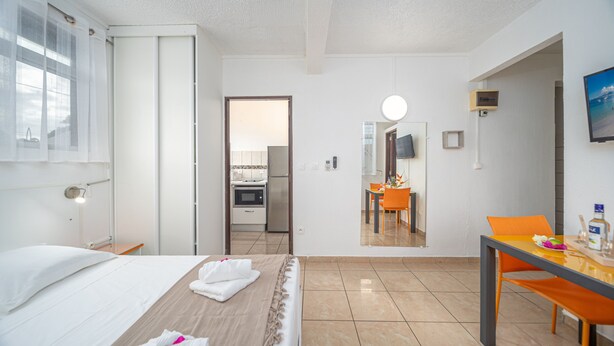Habitación de hotel con cama, una mesa de comedor con sillas, zona de cocina y baño visible a través de una puerta abierta.