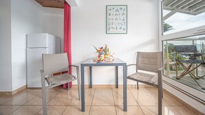 A room with a table, two chairs, a refrigerator, and a window with a view. - Studio 204 - Vanille - Proche plage (Les Trois-Îlets)