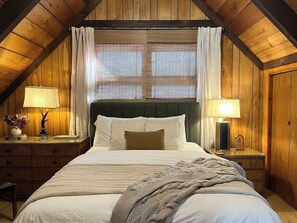 Una camera da letto con un letto grande, due comodini con lampade, una testiera e una finestra con tende.