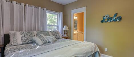 Un dormitorio con cama, mesita de noche, lámpara, ventana con cortinas, espejo y un cartel en la pared que dice "Lake".