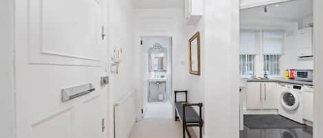 A hallway leading to a bathroom with a mirror, a bench, and a chandelier.