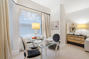 A hotel room with a glass dining table, two chairs, a dresser, and a window with curtains. - Luxury lower ground floor apt near King’s Road (London)