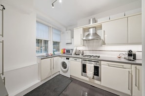 A modern kitchen with white cabinetry, a built-in washing machine, a stove, and a microwave. - Luxury lower ground floor apt near King’s Road (London)