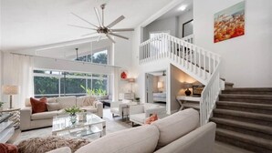 A spacious living room with a high ceiling fan, a staircase, and large windows. - CENTRALLY located house. (Naples)